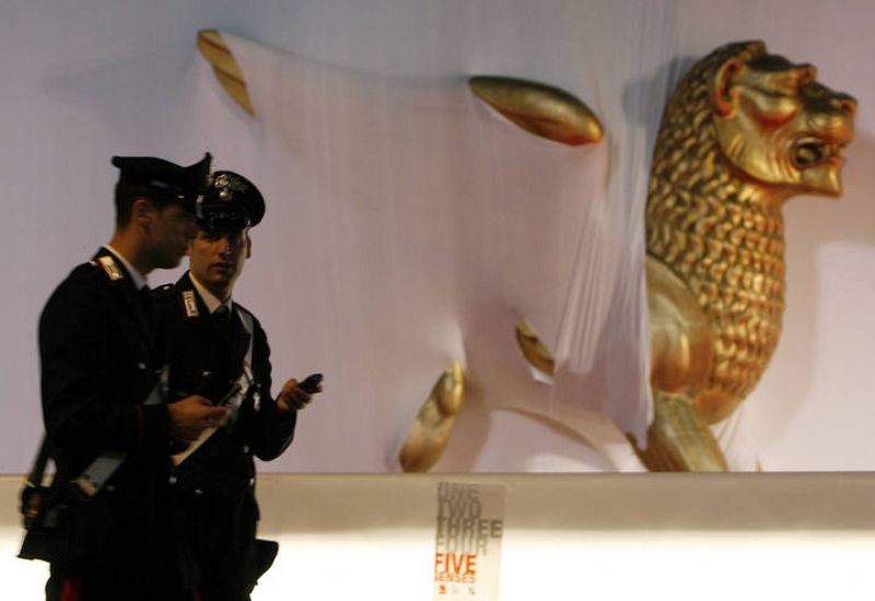 Two Carabiniers walk past a golden lion statue in front of the Cinema Palace in Venice