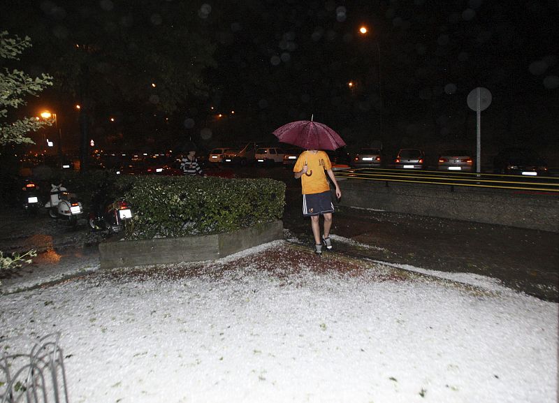 Curiosa imagen de un transehúnte vestido con ropa de verano ante la granizada caída esta noche en Madrid.