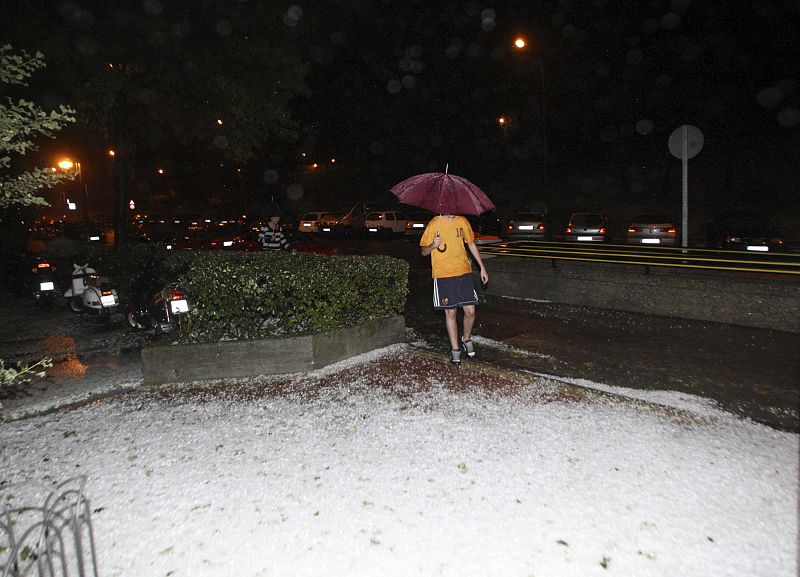 Curiosa imagen de un transehúnte vestido con ropa de verano ante la granizada caída esta noche en Madrid.