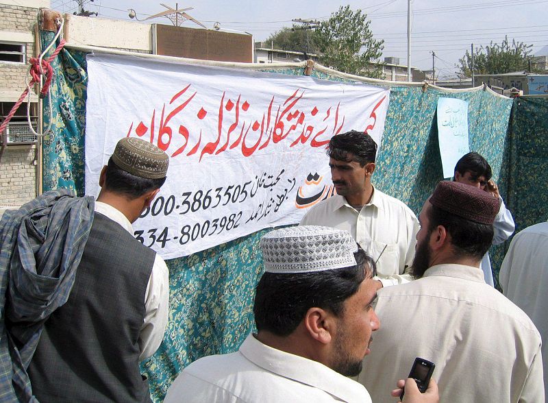 Varias personas reunidas junto a un cartel en el que se puede leer "Campo de ayuda para víctimas del terremoto" en Quetta, capital de la provincia de Balochistan (Pakistán).