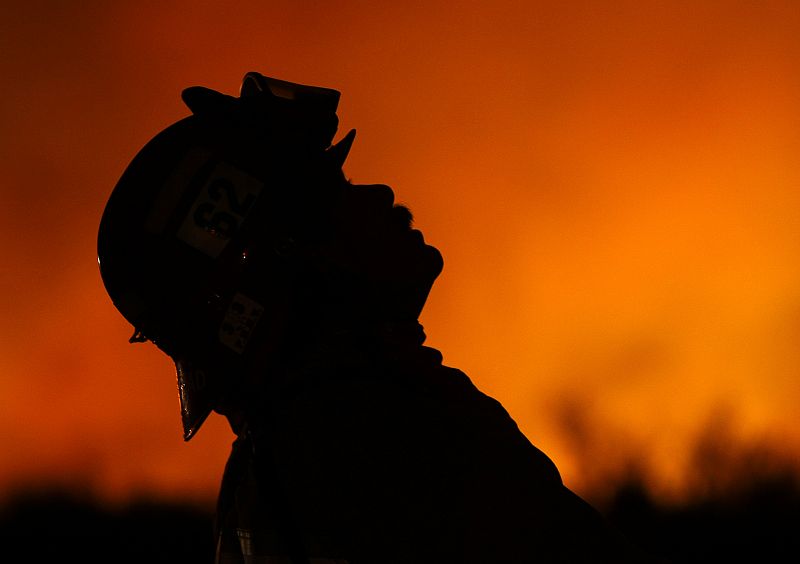 A fire fighter keeps watch on burning embers as fire fighters hold a fire line along Carbon Canyon road near Brea, California