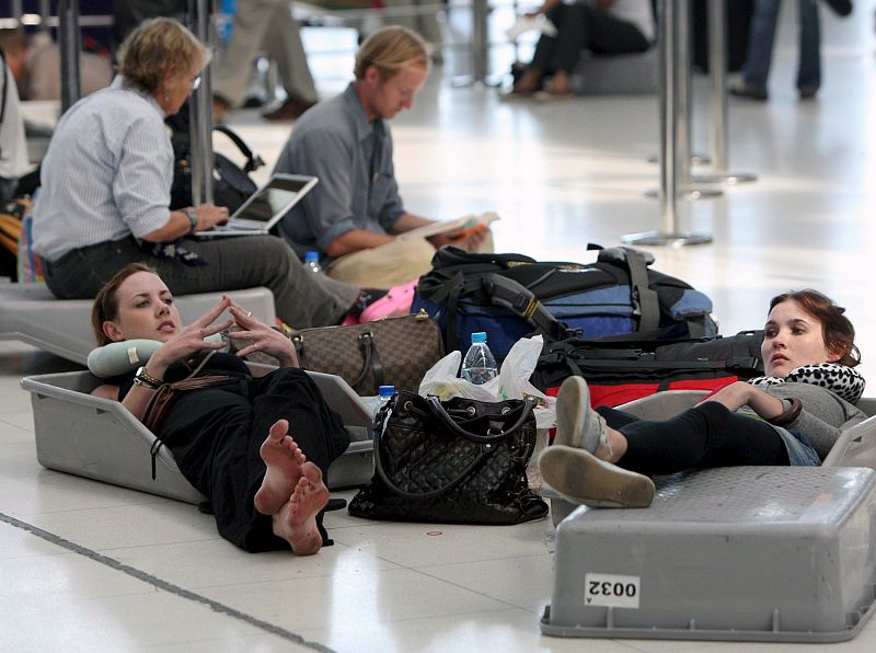 Pasajeros extranjeros esperan junto a su equipaje la salida de sus vuelos en el aeropuerto internacional de Bangkok.