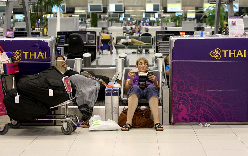 Dos pasajeras descansan y leen sobre una cinta transportadora de maletas del aeropuerto internacional de Bangkok (Tailandia).