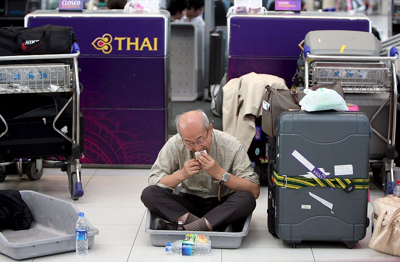 Un pasajero come un refrigerio junto a su equipaje mientras espera la salida de su vuelo en el aeropuerto internacional de Bangkok, que suspendió este miércoles de forma temporal todos los vuelos de entrada y salida a causa de la falta de seguridad t