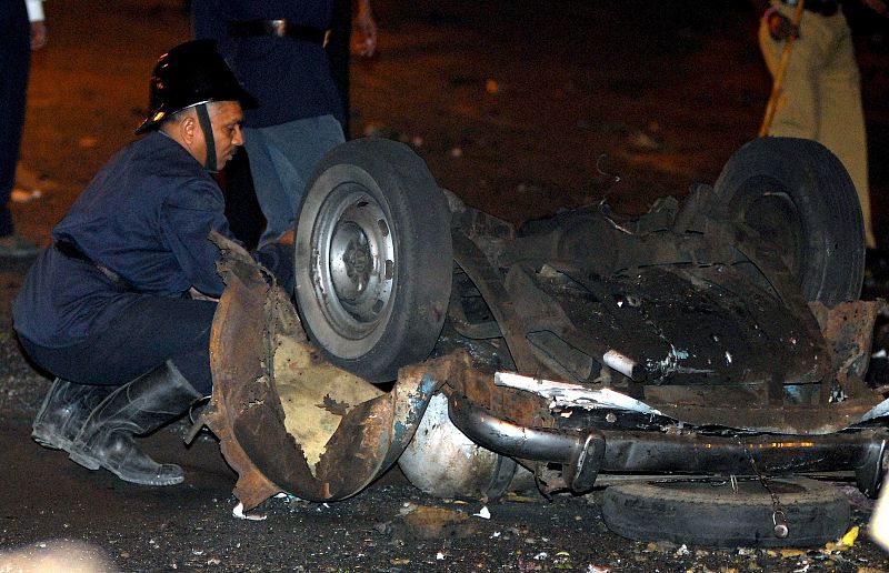 Un agente de seguridad examina los restos de un coche tras la serie de explosiones y tiroteos que ha tenido lugar en varios puntos del sur de la ciudad india de Bombay.