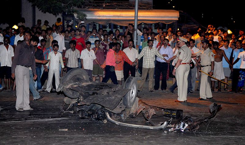 Varias personas observan los restos de un coche tras la serie de explosiones y tiroteos dirigidos contra una estación de trenes y dos hoteles de lujo, el Oberoi y el Taj Mahal.