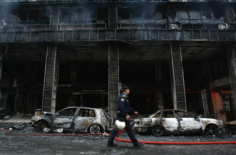 A policeman walks in front of a burnt building following riots in Athens