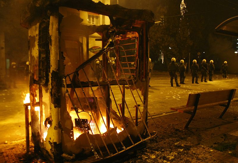 Policemen take up positions as a bus station booth is on fire during riots in Athens