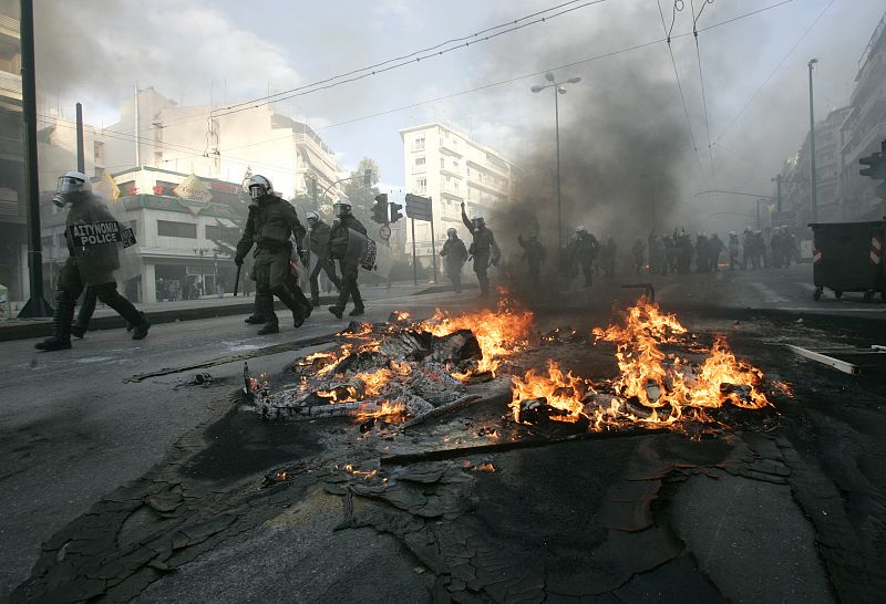 Los agentes caminan entre los restos de barricadas ardiendo en Atenas.