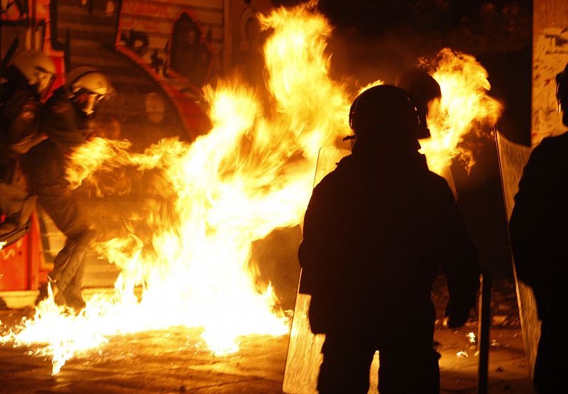 Los policías se protegen de un cóctel molotov durante los disturbios de Atenas