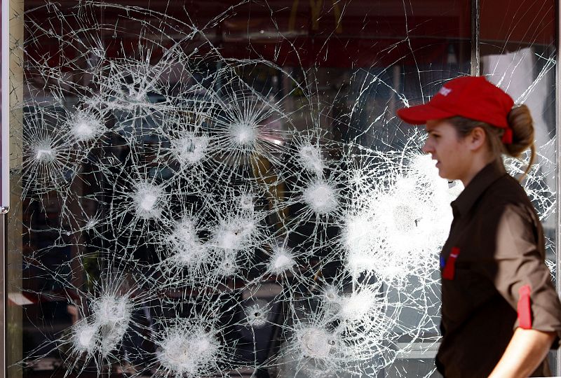 Una empleada de un McDonald pasa por delante del escaparate roto en Atenas.