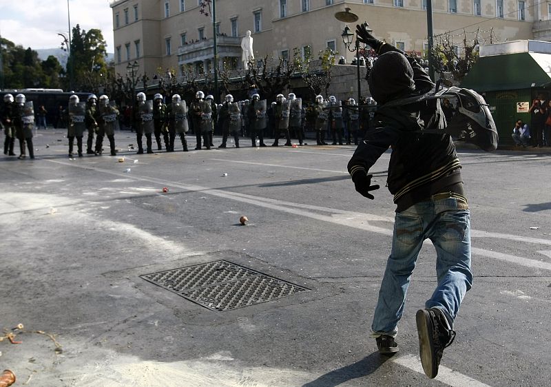 A protester throws a stone at policemen guarding Greece's parliament in Athens