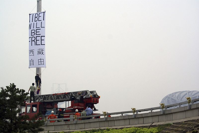 Un manifestante desciende de un poste después de colocar una pancarta en la que pedía 'Libertad para Tibet'