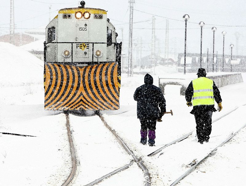 Dos operarios se acercan a una locomotora en las vias cubiertas por la nieve de la estación de Mataporquera, debido a las intensas nevadas que están cayendo en las zonas interiores de la cornisa cantábrica.