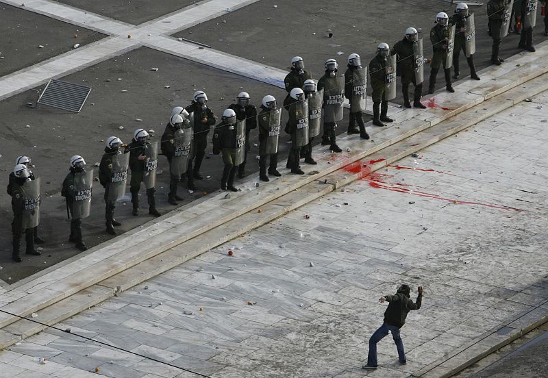 Un manifestante lanza piedras a la policía que protege las inmediaciones del Parlamento griego en Atenas. Se cumple una semana de la muerte del joven de 15 años por un disparo de la policía, suceso que originó la oleada de violencia.