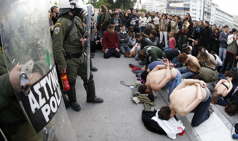 Un grupo de manifestantes se arrodilla ante los policías que protegen el Parlamento griego de las manifestaciones y disturbios que se están repitiendo desde la muerte hace una semana de un joven por un disparo policial.