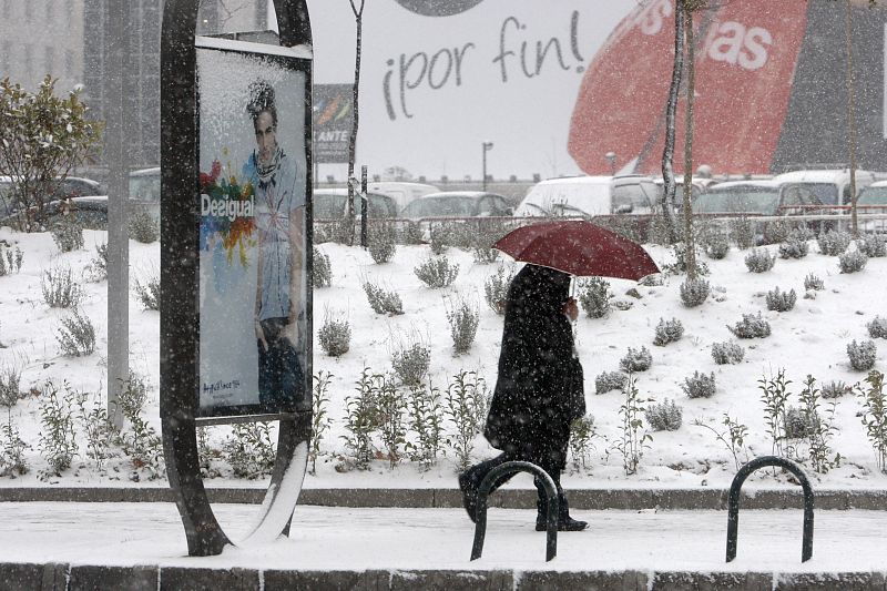 Un hombre se guarece de la nieve en el Paseo de la Castellana de Madrid.