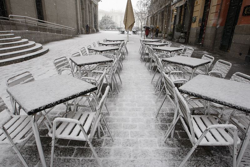 Las sillas y mesas de un café sito en las inmediaciones del Teatro Real, con el Palacio Real al fondo, durante la intensa nevada.