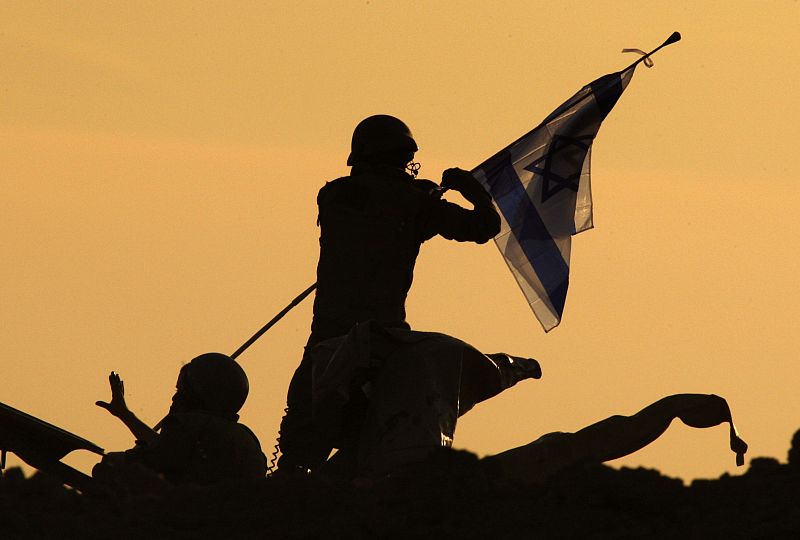 Israeli soldier adjusts flag atop mobile artillery unit outside northern Gaza Strip