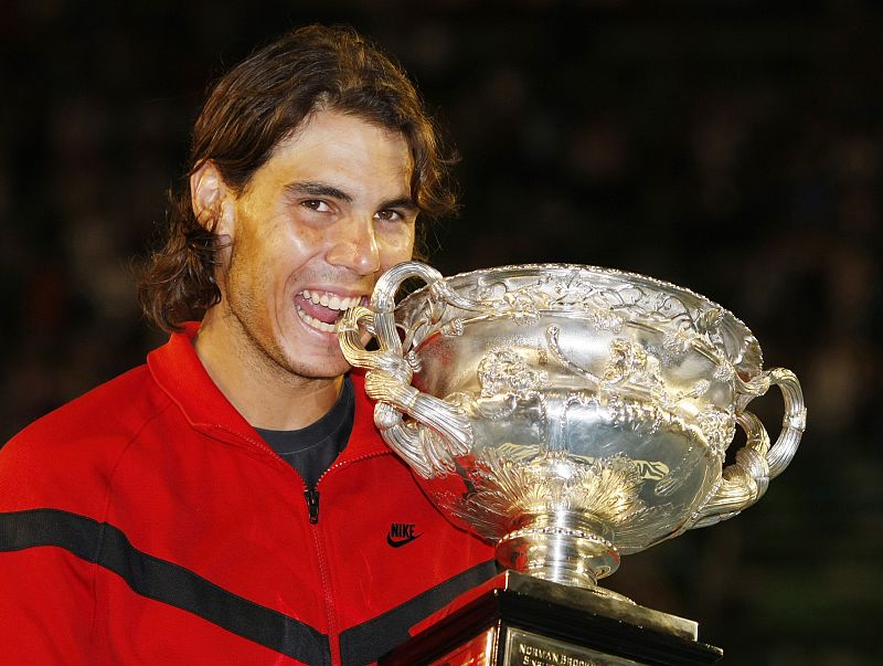 Spain's Nadal bites the trophy as he poses after winning his men's singles final match against Switzerland's Federer at the Australian Open
