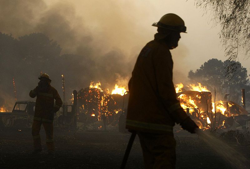 Firemen extinguish a bushfire while a shed burns on the outskirts of Labertouche