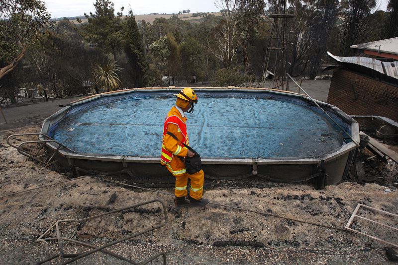 Un bombero inspecciona el jardín de una vivienda que ha quedado reducida a ruinas.