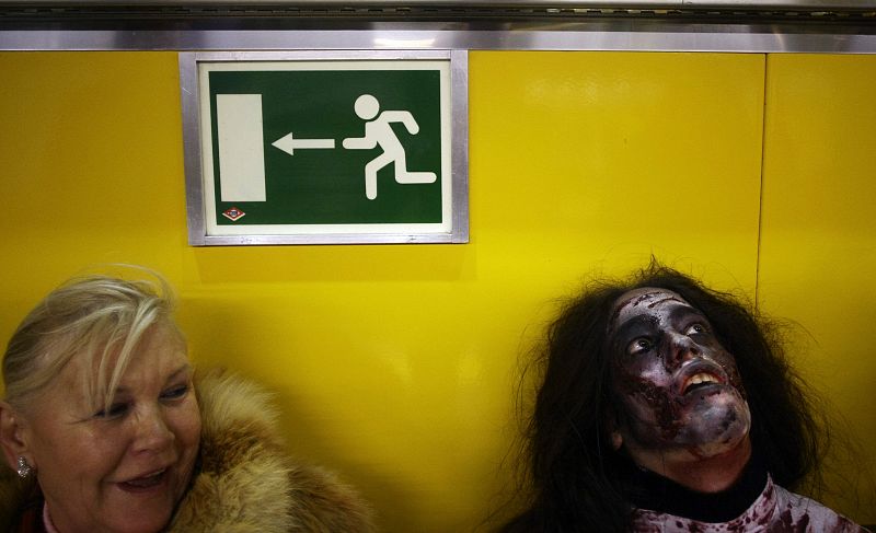 A woman looks at a man dressed like a zombie at a subway station in Madrid
