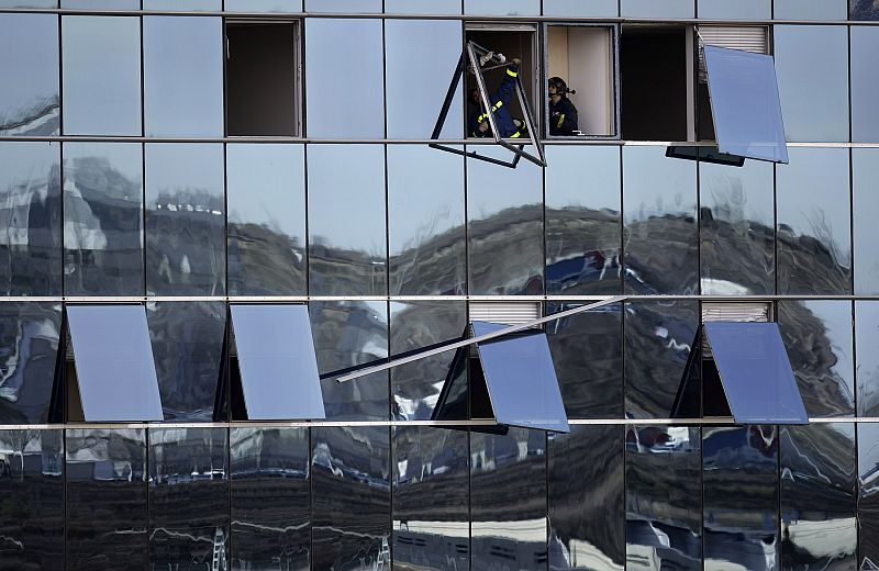 Un grupo de bomberos trabaja quitando las ventanas rotas en uno de los edificios dañados tras la explosión.