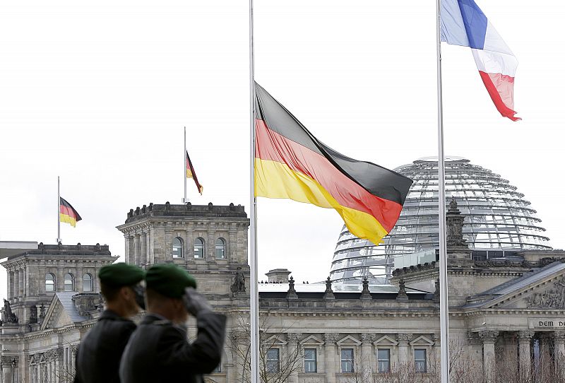 German soldiers salute next to a German national flag that has been set half-mast before a regular meeting of French and German ministers in Berlin