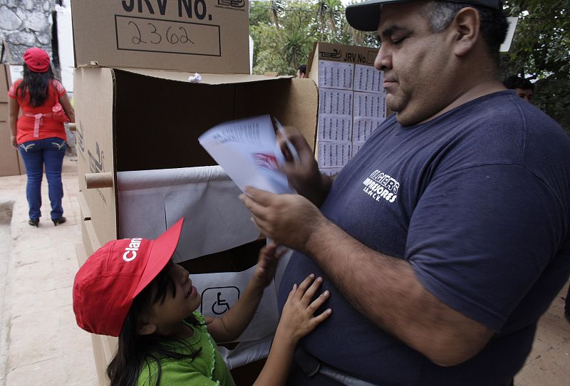 Una chica salvadoreña observa a su padre metiendo su papeleta en la urna en Panchimalco, cerca de San Salvador.