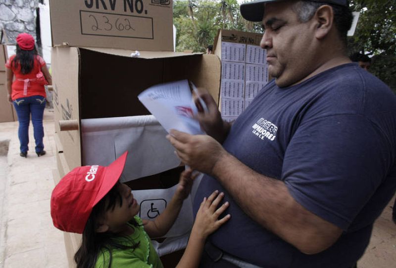 Una chica salvadoreña observa a su padre metiendo su papeleta en la urna en Panchimalco, cerca de San Salvador.