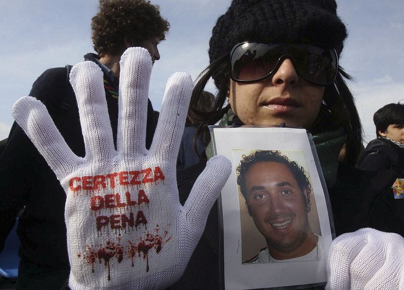 Demonstrator displays glove with phrase "Punishment must be guaranteed" as she holds picture her parent killed by mafia in Naples