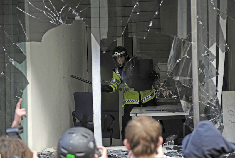 Un agente permanece detrás de la ventana rota de una oficina del Royal Bank of Scotland en Londres.