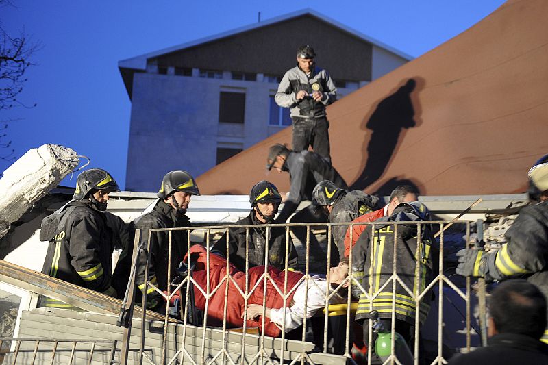 Rescue workers carry an injured woman away from her house in Aquila