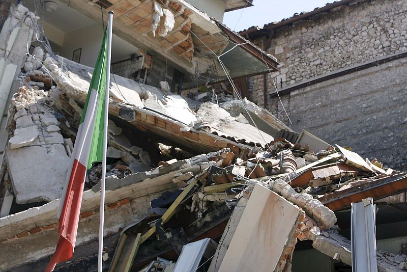 Una bandera de Italia junto a un edificio reducido a escombros