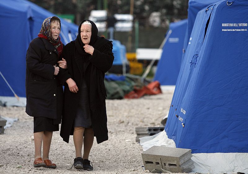 Dos mujeres mayores caminan entre las tiendas en las que han pasado la primera noche en Paganica.
