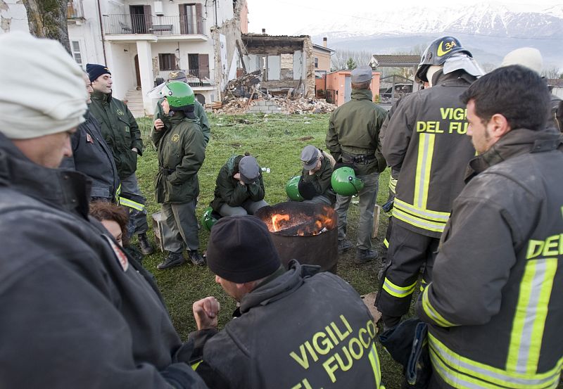 Un grupo de personas que trabaja en el rescate de víctimas se calientan con una hoguera en Onna.