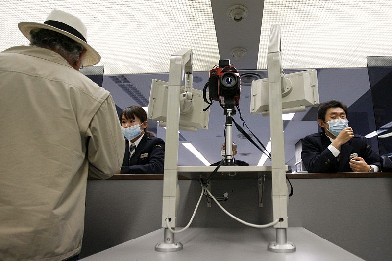 Dos inspectores cubiertos con mascarillas comprueban la temperatura corporal de los pasajeros de un avión con un escáner térmico en la puerta de llegadas del aeropuerto internacional de Narita