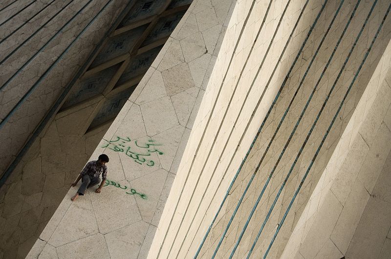 Un hombre sube un monumento de la plaza de Azadi