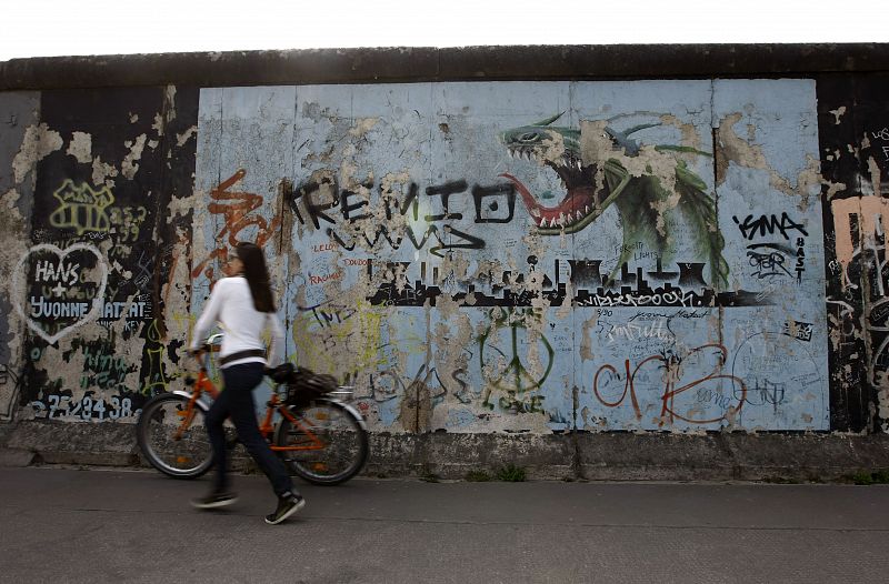 A woman pushes her bicycle past a graffiti covered section of the former Berlin wall