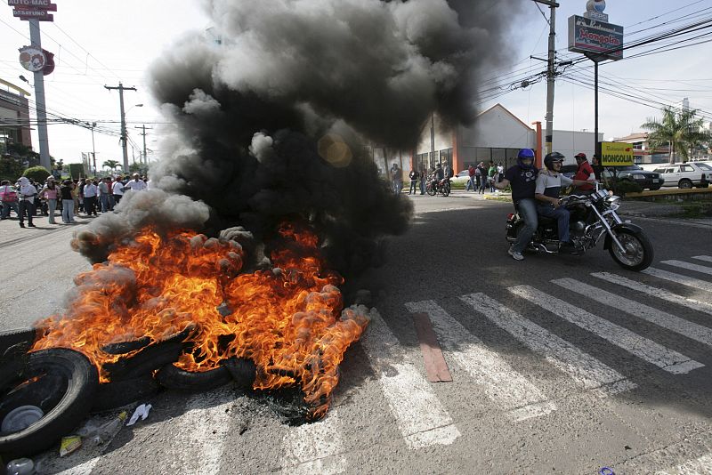 Supporters of Honduras' President Zelaya ride on a motorcycle past burning tires near the presidential residency in Tegucigalpa