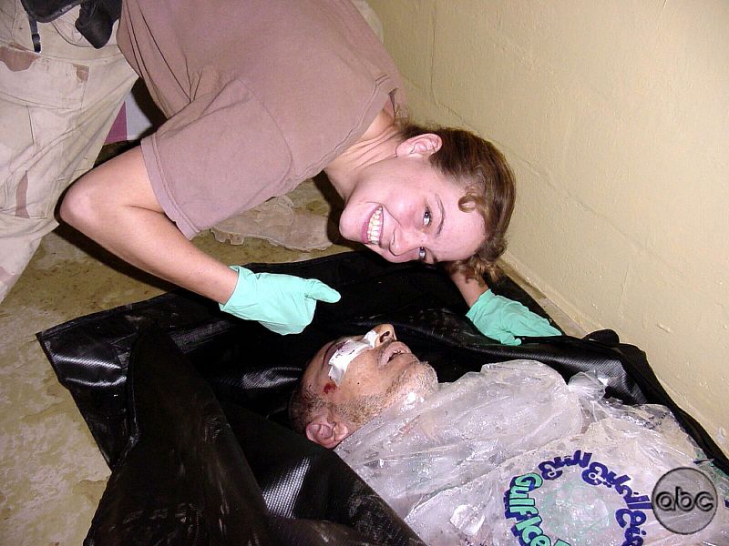 A WOMAN IDENTIFIED AS SPC HARMAN POSES OVER A BODY AT ABU GHRAIB.