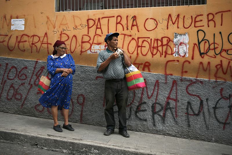 Hondureños esperando el autobús frente a una pared llena de pintadas en Tegucigalpa