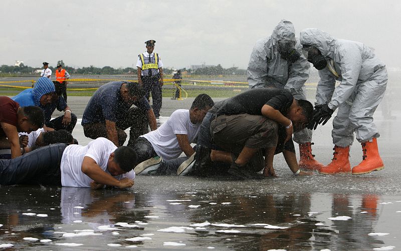 Rescuers in protective suits assist workers acting as airline passengers during emergency exercise on tarmac of Ninoy Aquino international airport in Manila