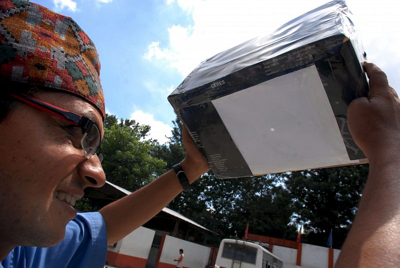 Jayanta Acharya, coordinador del comité organizador de la visión del eclipse solar, usa una caja de reflejo para ver el sol durante la celebración de una clase de preparación sobre cómo ver el eclipse solar en Katmandú (Nepal).