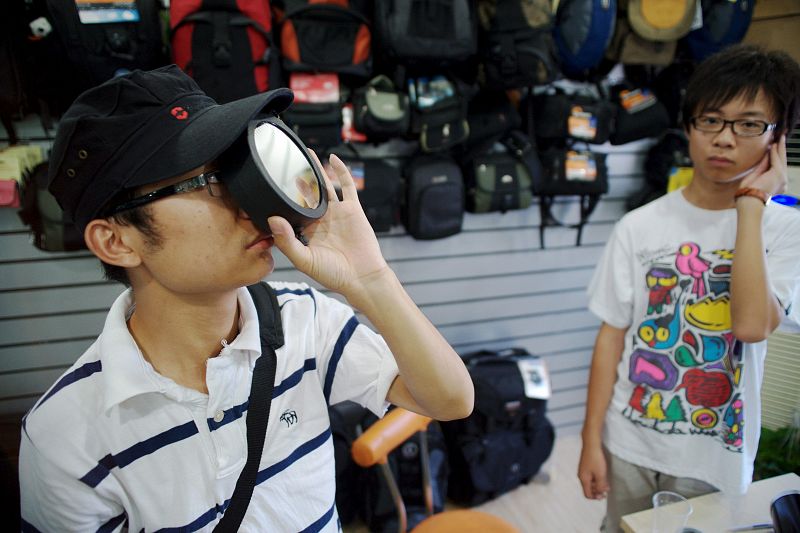 Un hombre prueba un filtro telescópico que se utiliza para observar eclipses solares, en una tienda de equipamiento fotográfico en la provincia china de Zhejiang.