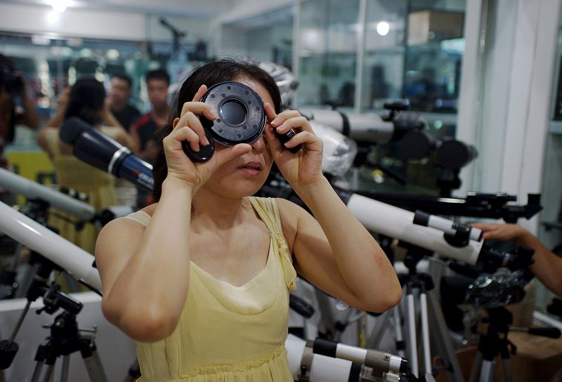 Una mujer prueba un filtro telescópico que se utiliza para observar eclipses solares, en una tienda de equipamiento fotográfico en la provincia china de Zhejiang.