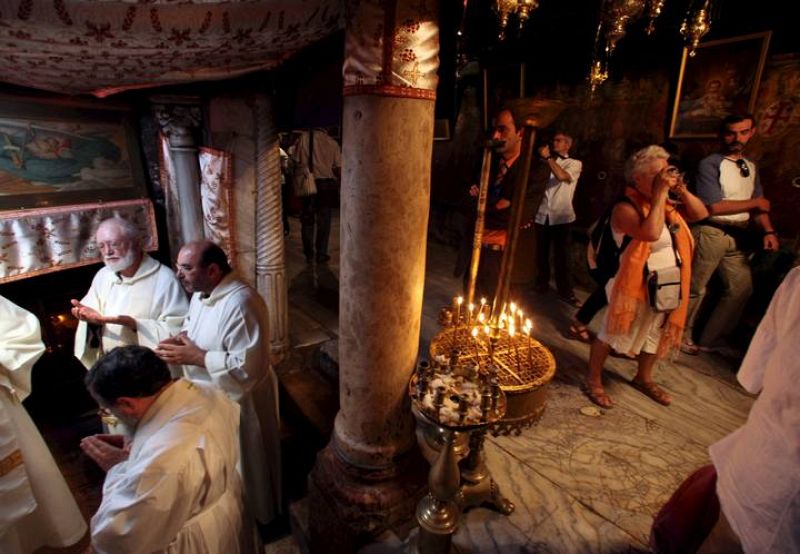 VARIOS SACERDOTES CRISTIANOS REZAN EN EL INTERIOR DE LA IGLESIA DE LA NATIVIDAD JUNTO A UN GRUPO DE TURISTAS