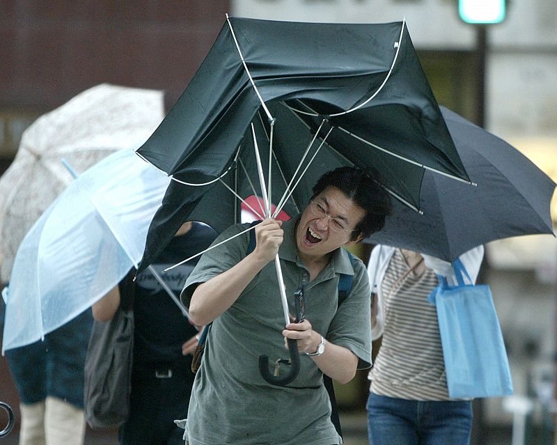 A MAN STRUGGLES WITH HIS UMBRELLA IN STRONG WINDS AND RAIN CAUSED BY