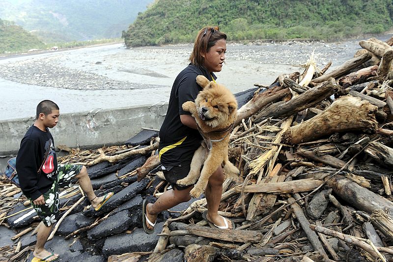 A woman carries a dog while walking with her son after leaving their home in a landslide-affected mountain village in Pingtung County